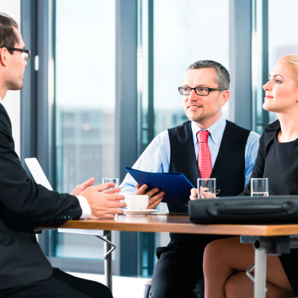 Business - young man in an Job interview, hands over his application papers to the boss and his female assistant in their office
